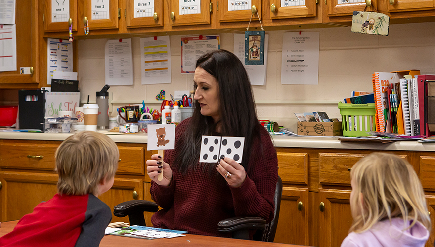 Female teacher sitting at a table showing two children flashcards in her hands