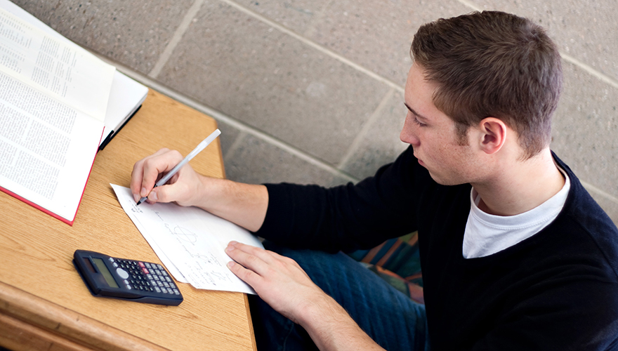 Male student writing at a desk with a calculator