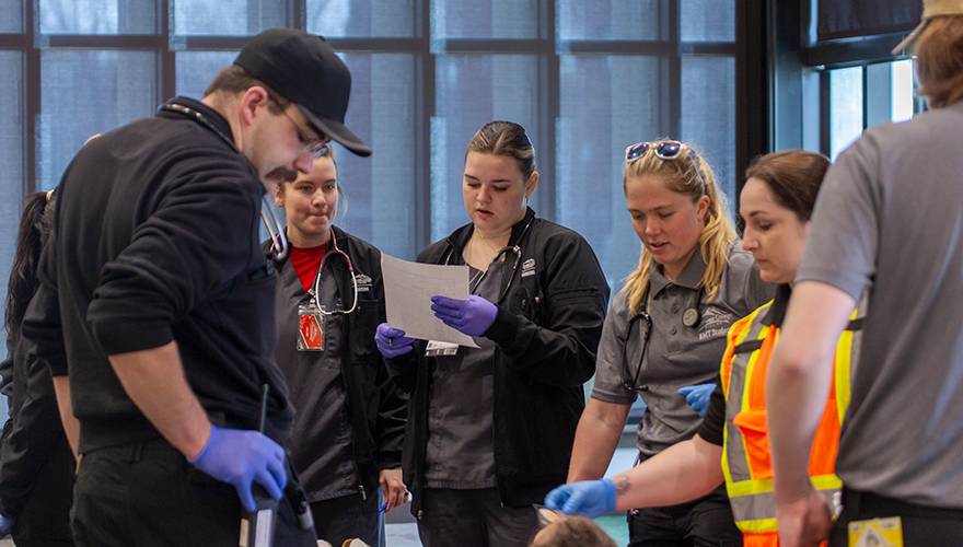 Group of nursing and EMS students wearing rubber gloves standing around a gurney holding a patient