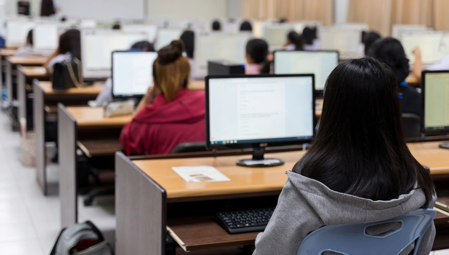 Students sitting a room filled with computer monitors and instructor at the front of the room