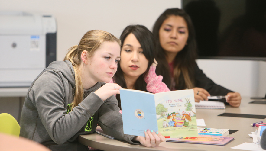 Female college students at a table looking a children's book