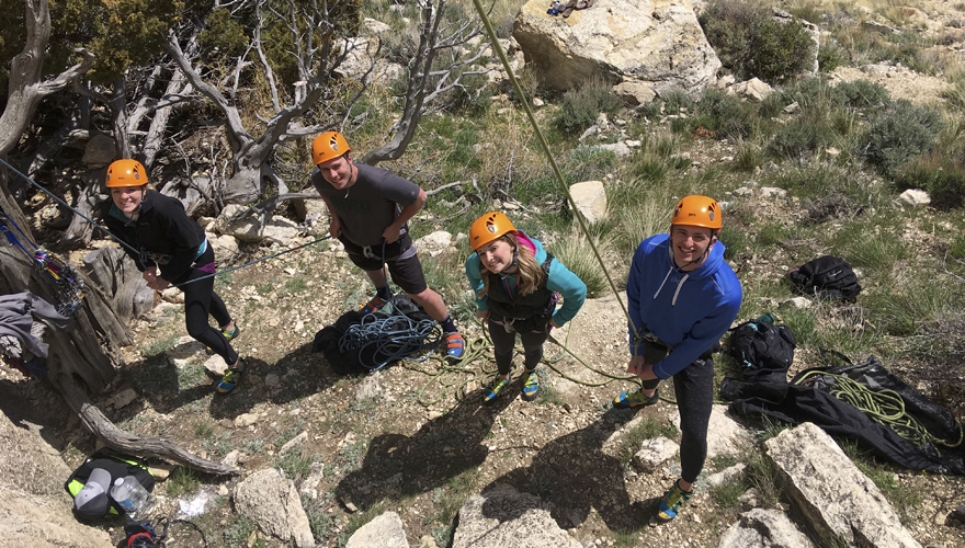 Group of four students in climbing gear and orange helmets looking up the ropes from ground level