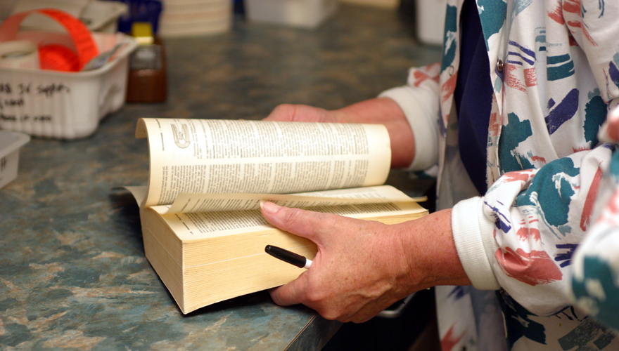 Woman's hands going through pages of a thick book resting on a table