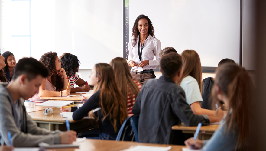 Female teacher standing in front of a whiteboard talking to a classroom of high school students