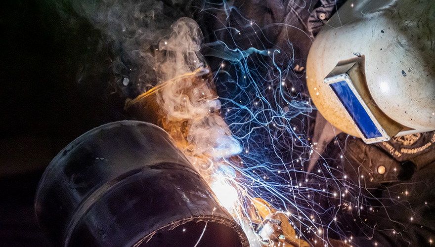 A welder in a heavy face shield leaning to the side of a welding project with sparks