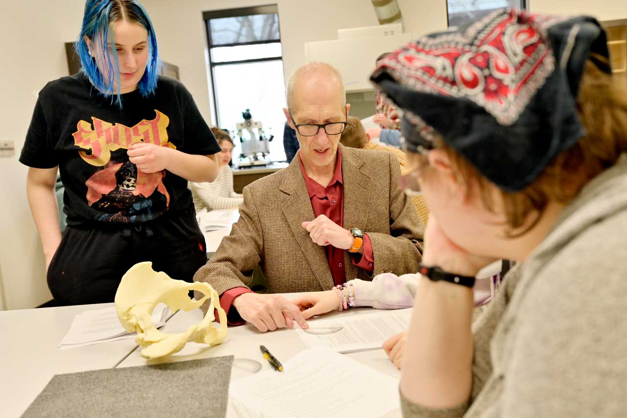 Professor pointing to a board with high school students watching