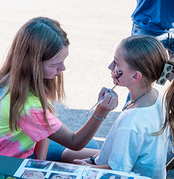A young girl getting her face painted by an older girl