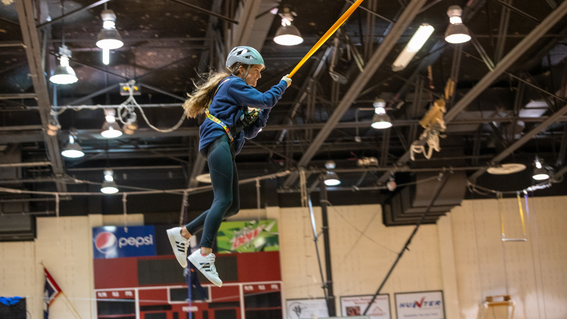 Female student swinging through the air on a rope in Cabre Gym