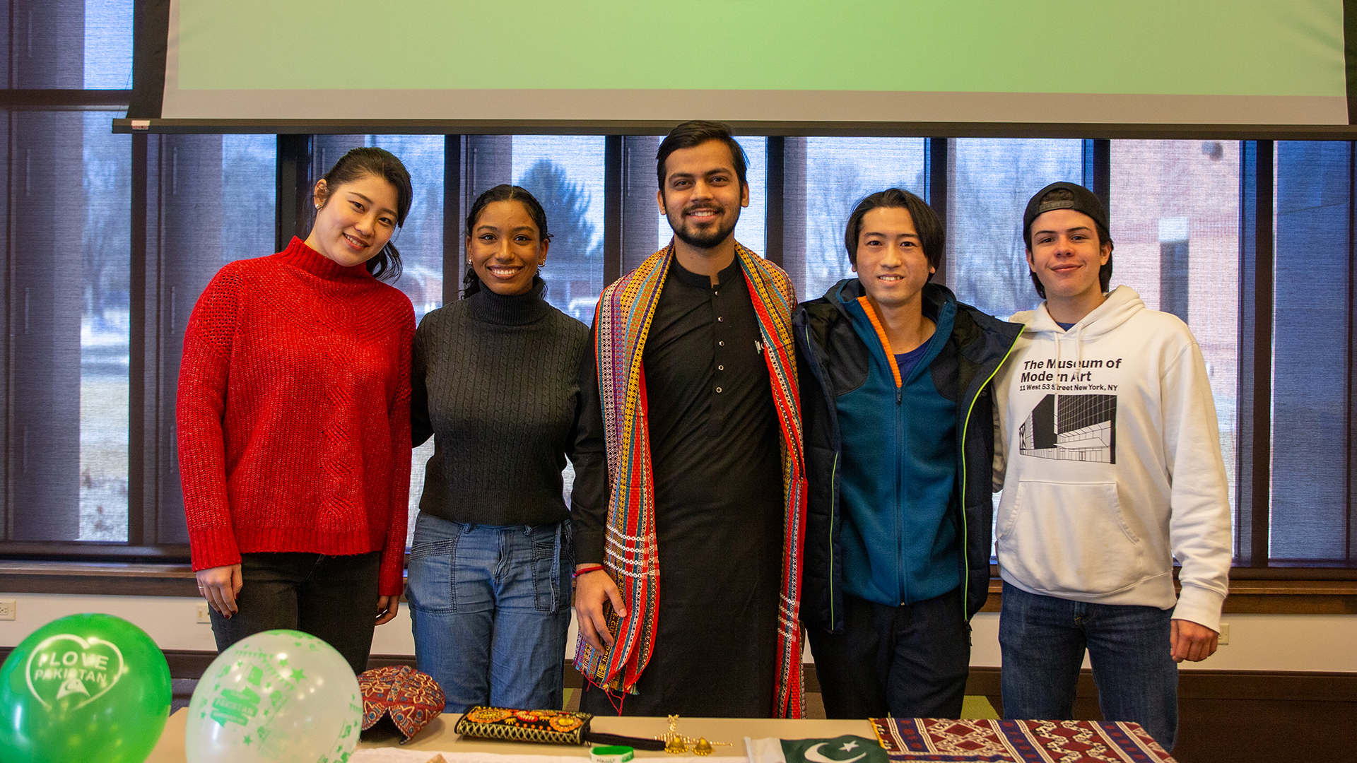 Five international students with arms around each other standing behind a table