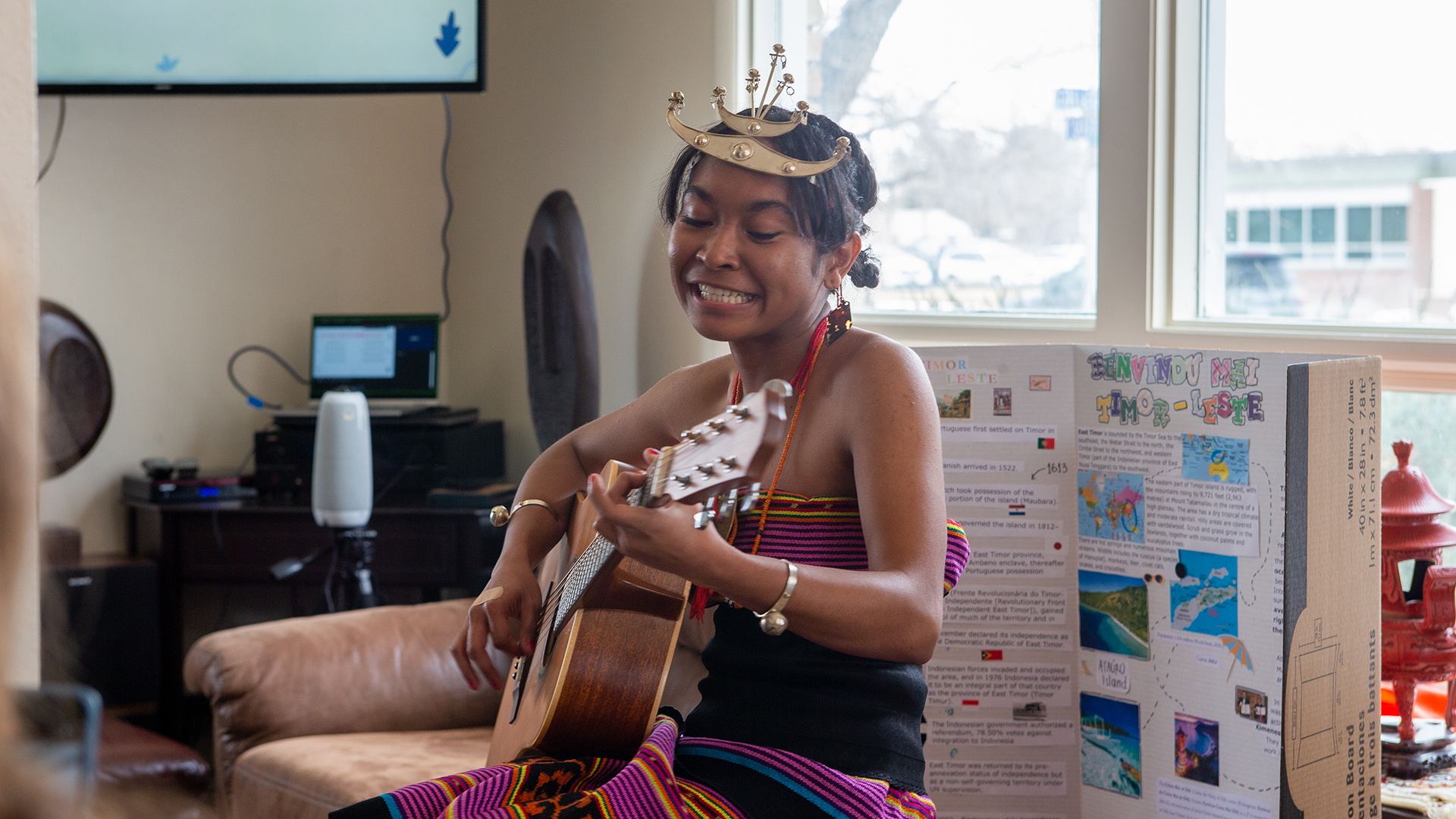 Female student from Timor Leste playing the guitar in a living room