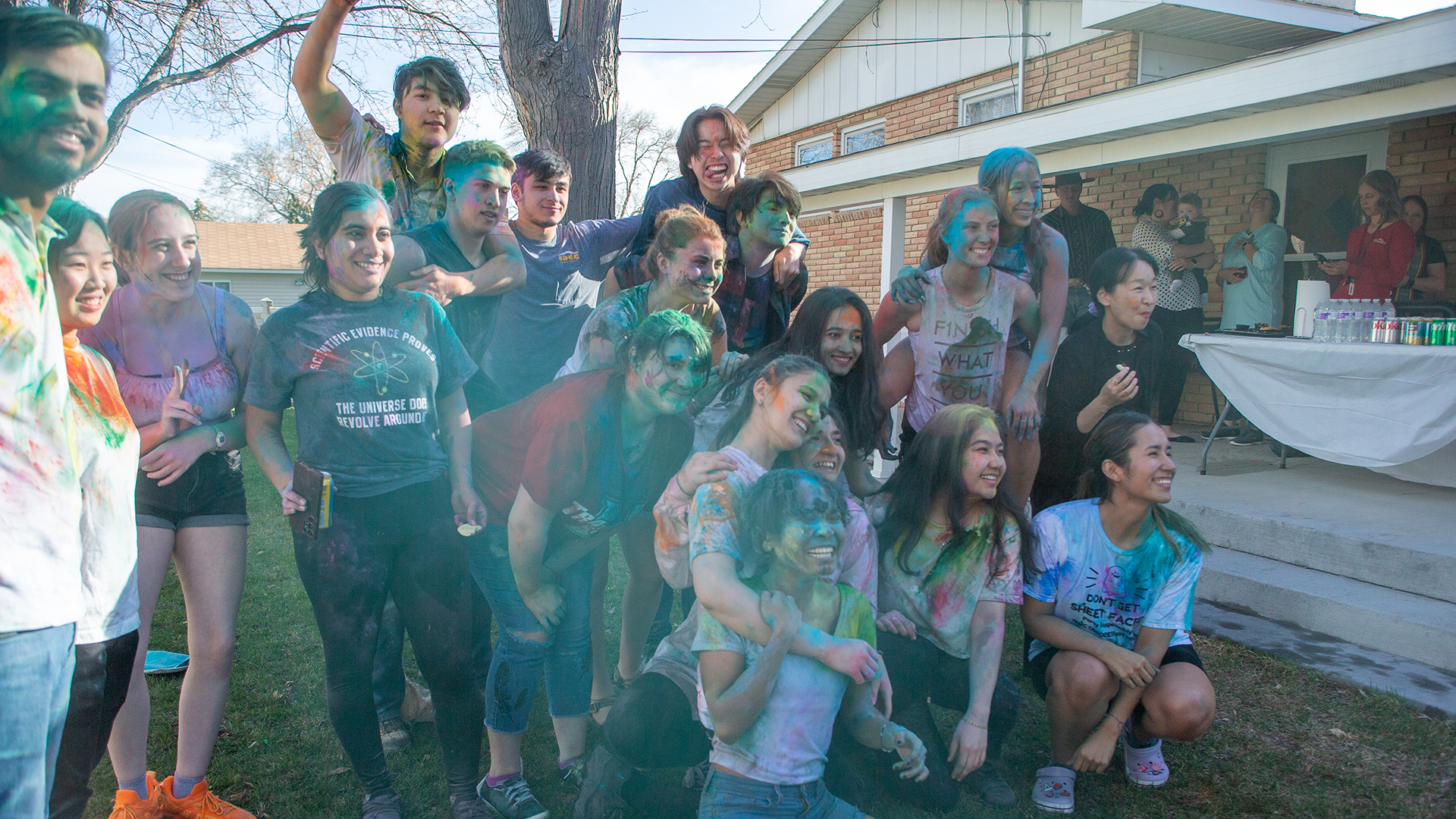 International students covered in colored powder celebrating Holi in the backyard of a house