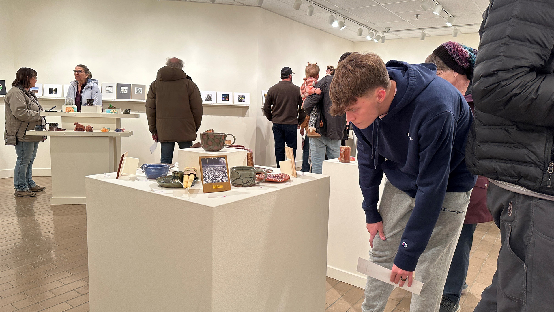 A male student crouched over looking at small artwork on a pedestal inside a gallery