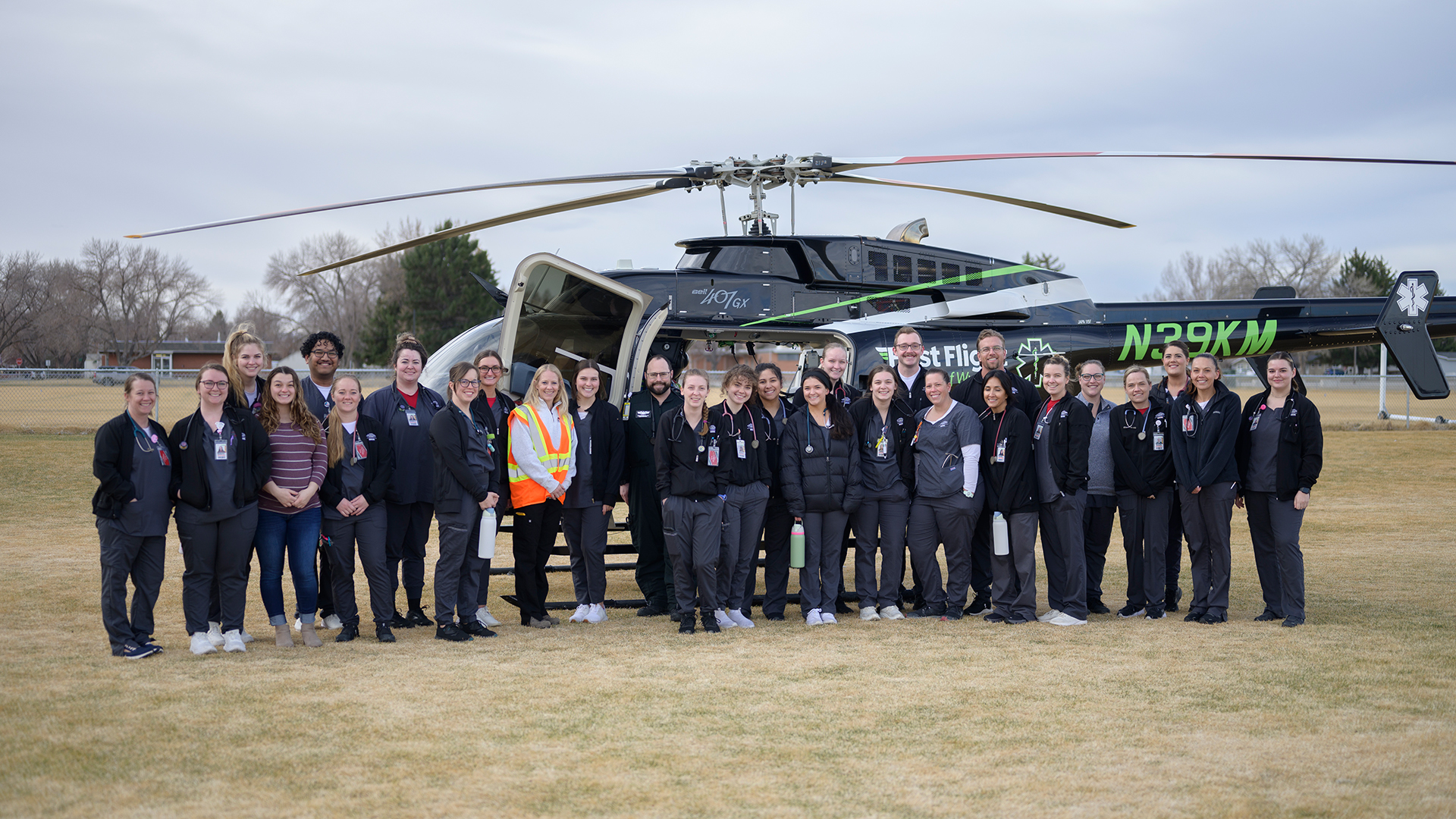 A large group of nursing students standing in front of a helicopter in a field