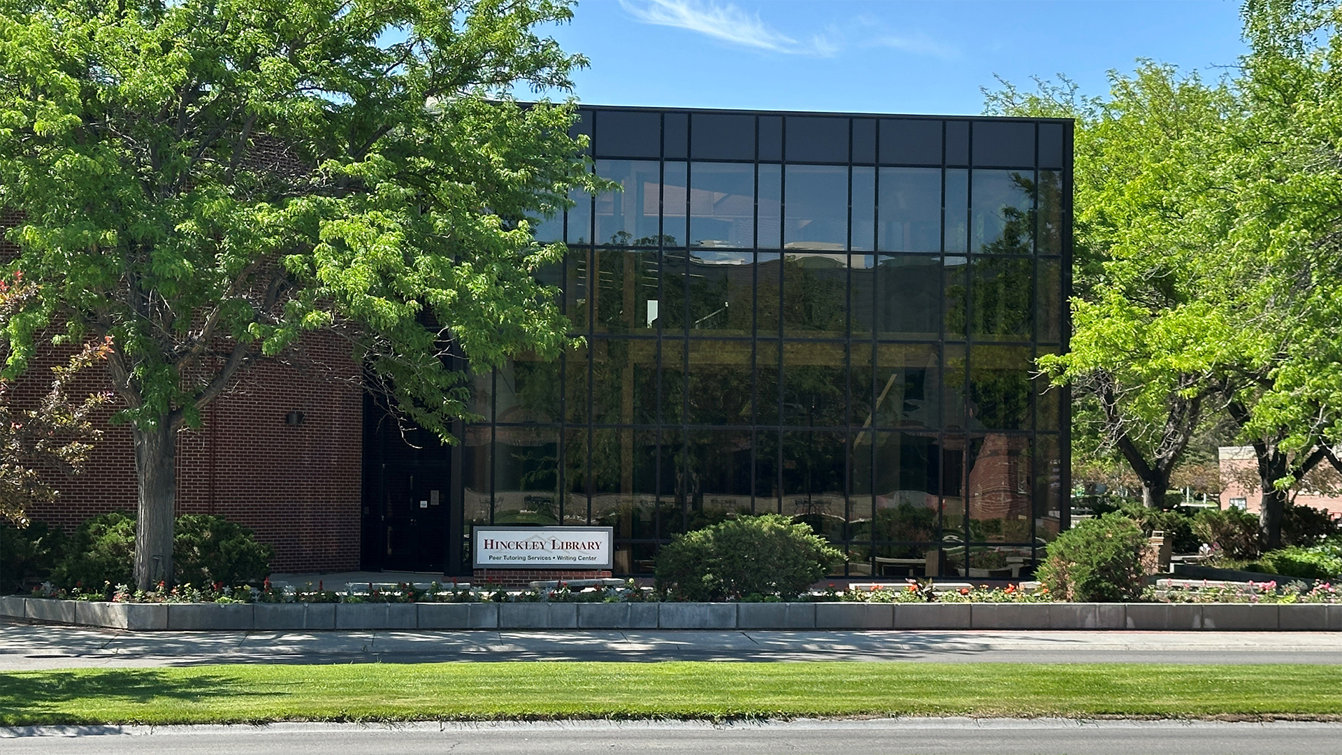 Across the street from Hinckley Library facing two story glass windows surrounded by green trees and flower beds