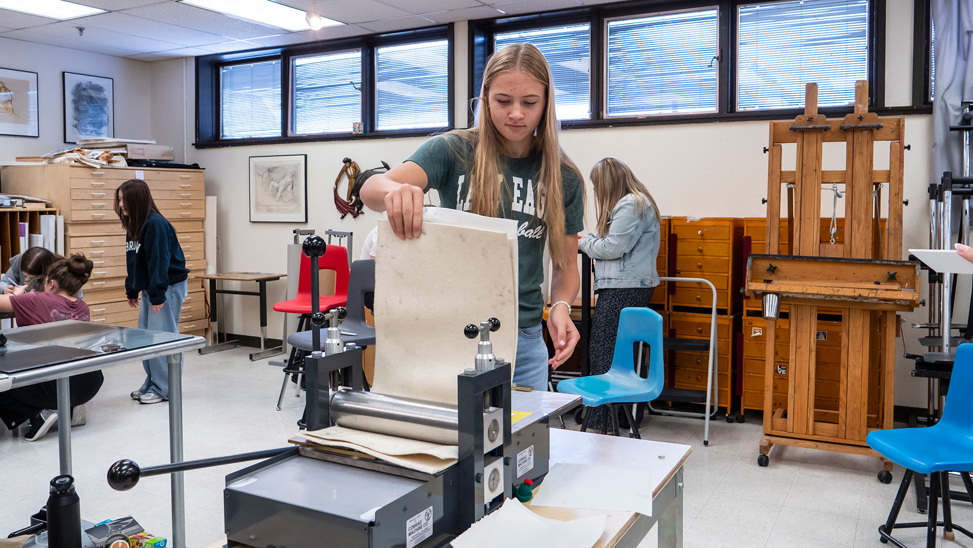 A female high school student working on a small printing press, holding up and looking at collection of papers