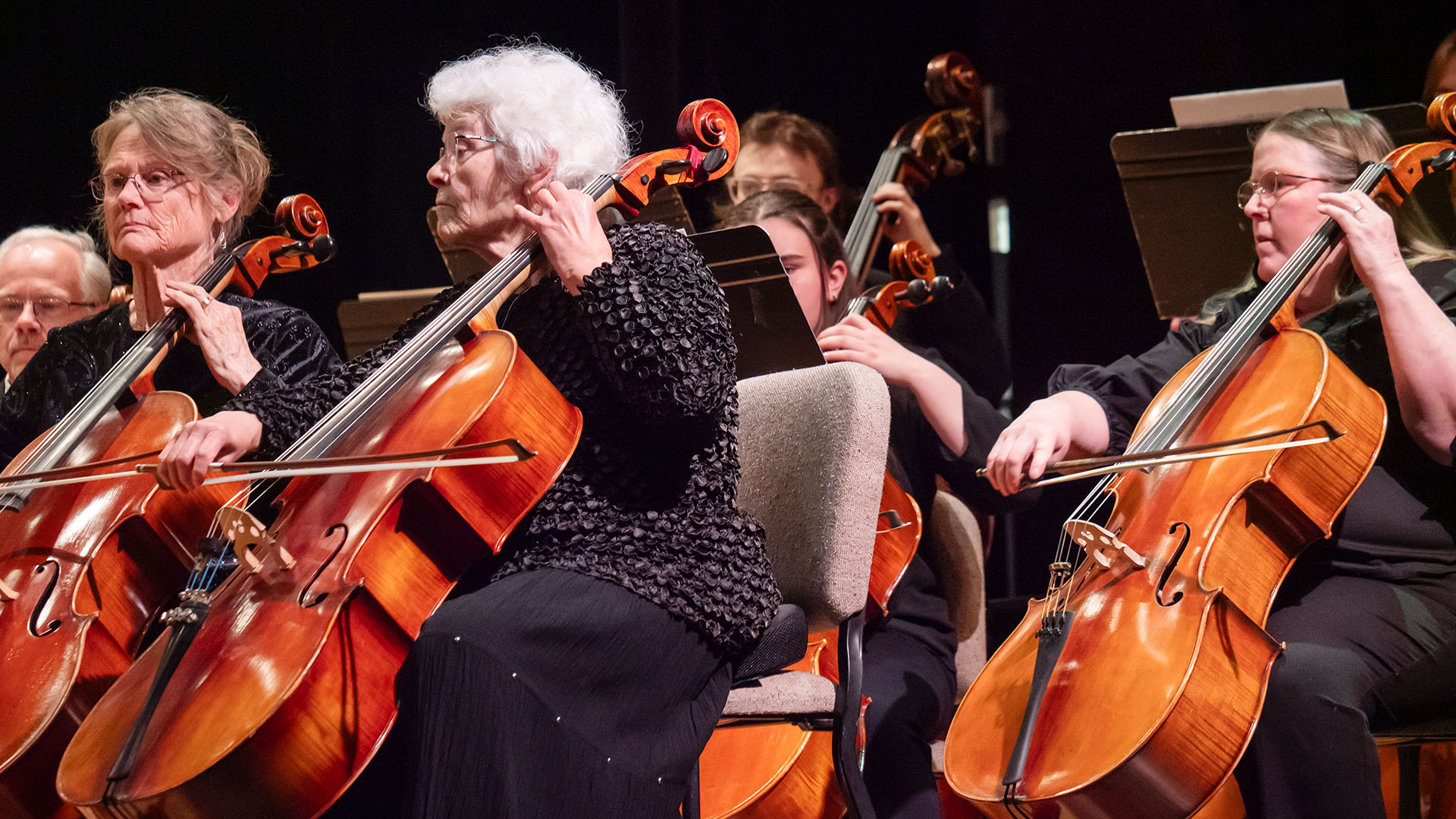 Three women playing cellos while sitting in chairs on a stage