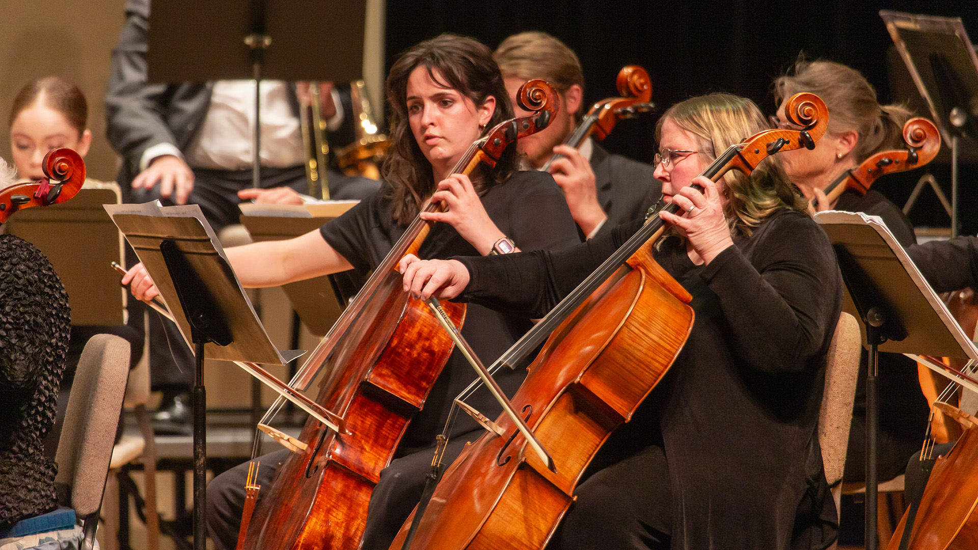 Two women sitting in chairs playing cellos in a concert