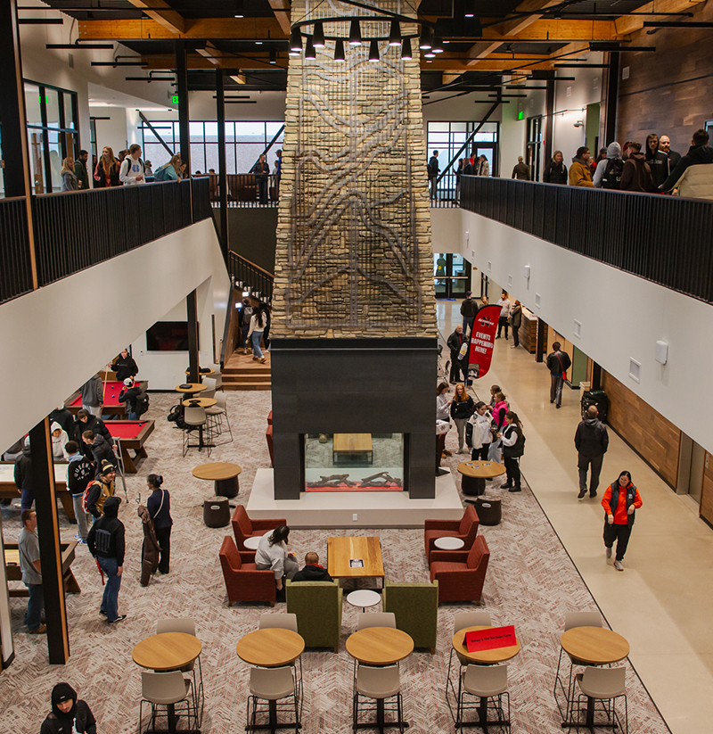 Second floor view of floor to ceiling fireplace with artwork on stone, all surrounded by talking people walking and sitting