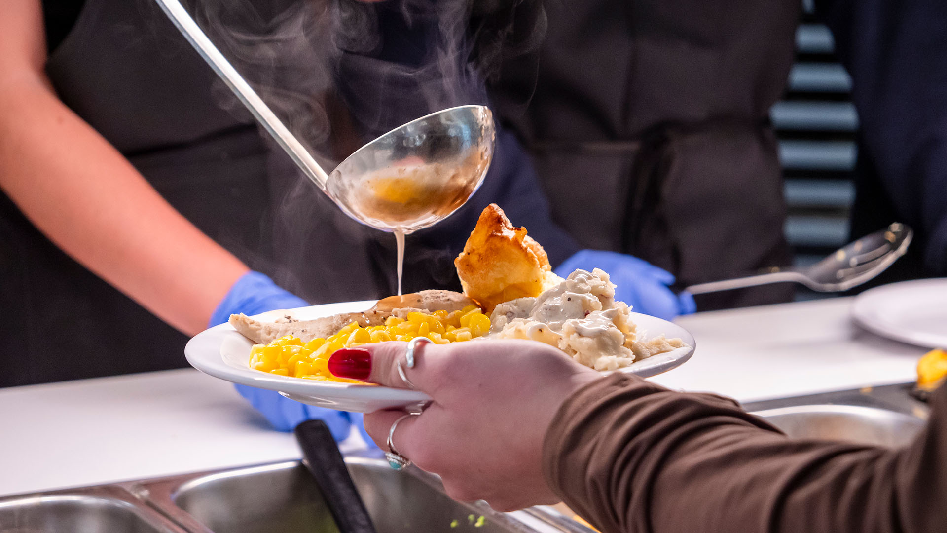 A close up picture of a person using a ladle to pour gravy over a meal on a plate held by a hand