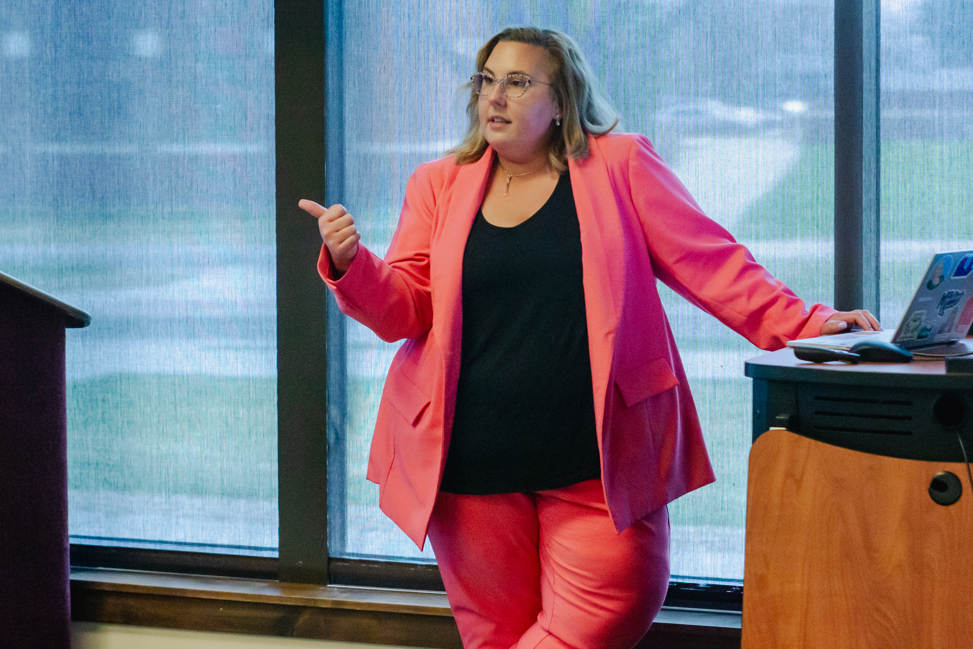 A professor standing next to a laptop and podium speaking to the audience