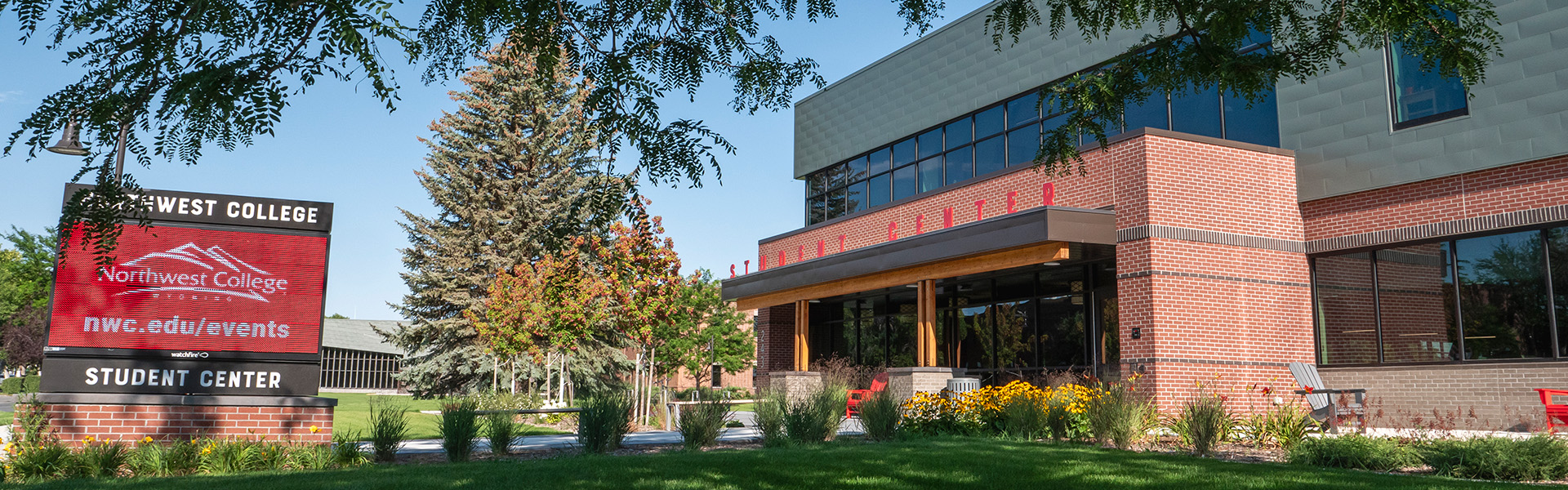 Front of the student center in summer looking up from ground level under a tree with message board on left