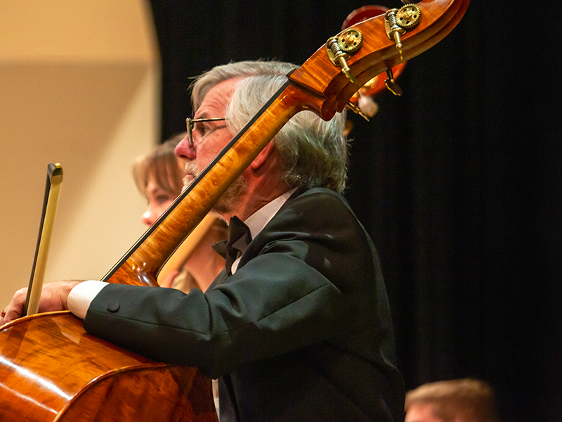 Close-up picture of a man sitting in a chair preparing to play a cello that is resting on his lap