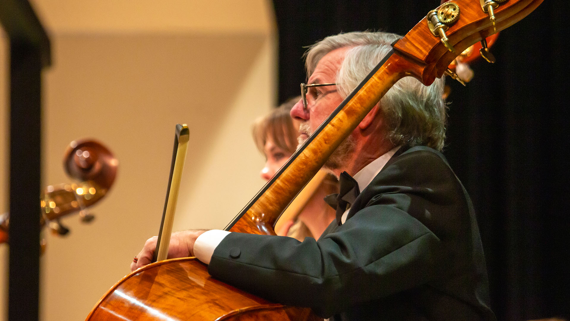 Close-up picture of a man sitting in a chair preparing to play a cello that is resting on his lap